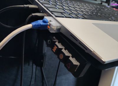A four-key keypad with non-specific symbol keycaps (two green, one orange, one red) mounted beneath the left side of the laptop tray, facing to the left.